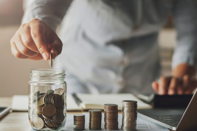 businesswoman saving money by hand puting coins in jug glass