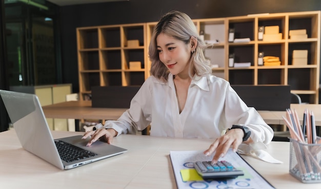 Businesswoman sitting working on laptop and use calculating machine analysis document income work invoice bill bank