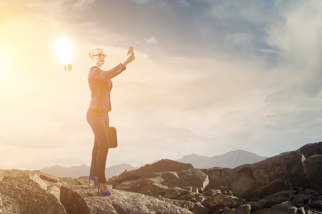 Businesswoman standing against landscape and making selfie. Mixed media