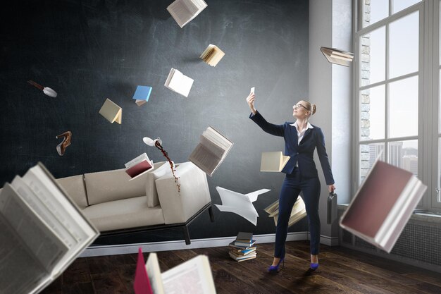 Businesswoman standing and making selfie with flying books all around her. Mixed media