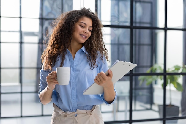 Businesswoman standing in the office corridor with documents and coffee