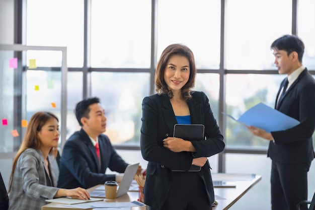 Businesswoman standing at the office with group of colleagues in background working on laptop computer