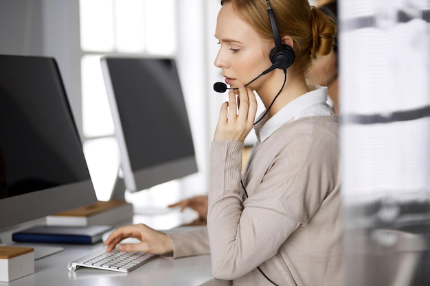 Businesswoman talking by headset while sitting in office. Call center and diverse people group in business.