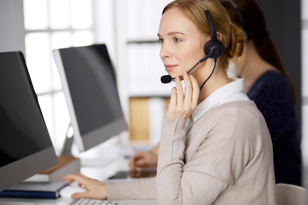 Businesswoman talking by headset while sitting in office. Call center and diverse people group in business.