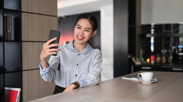 Businesswoman talking on video call on smartphone with her friends in office.