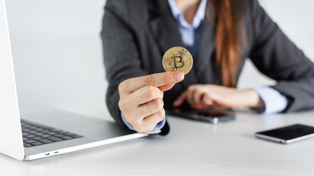 Businesswoman trader holding bitcoin cryptocurrency in the office with laptop and smartphones