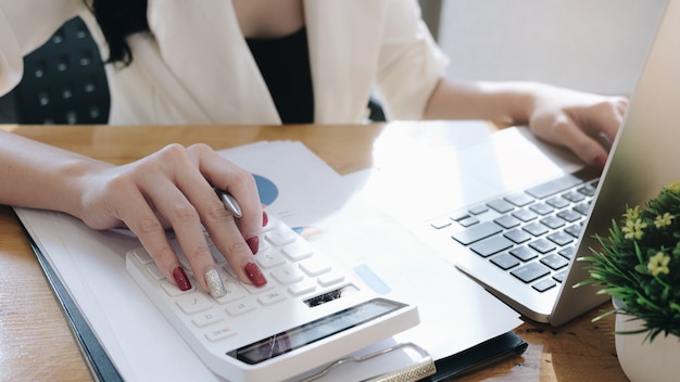 Businesswoman using calculator and laptop for do math finance on wooden desk in office.