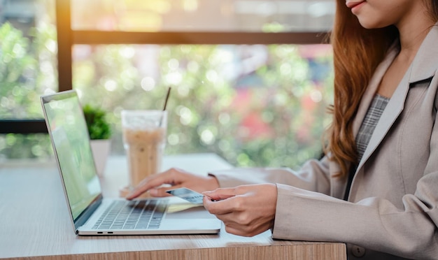 Businesswoman using credit card for online shopping. Woman with technology on computer in cafe alone.