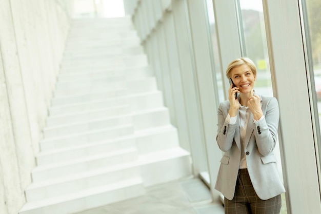 Businesswoman using mobile phone on modern office hallway