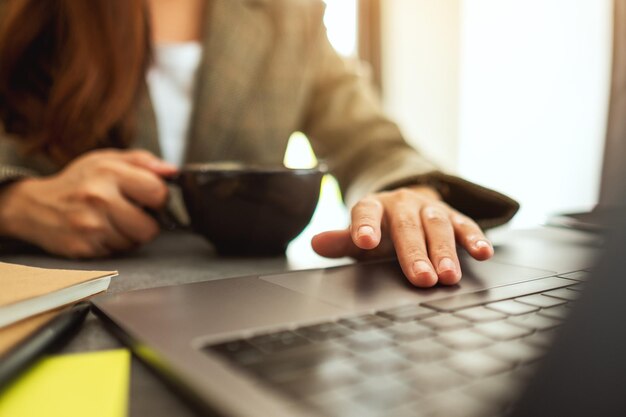 Businesswoman using and touching on laptop touchpad while drinking coffee in office