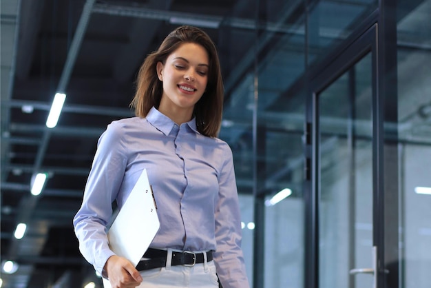 Businesswoman walking along the office corridor with documents