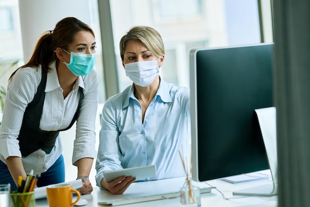 Businesswoman wearing face masks and cooperating while working on desktop PC in the office