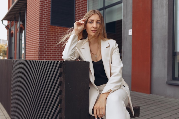 businesswoman in white elegant suit sitting on bench near business center