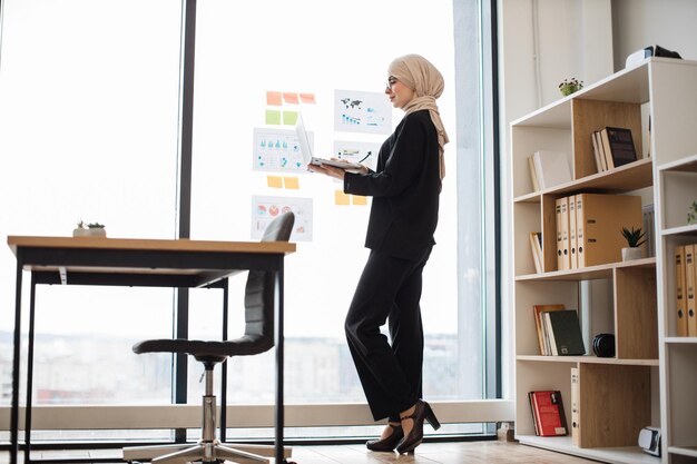 Businesswoman with laptop viewing data visuals on glass