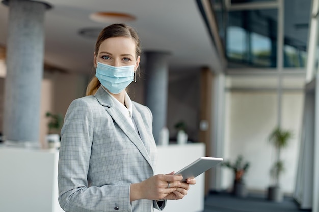 Businesswoman with protective face mask using touchpad in a hallway