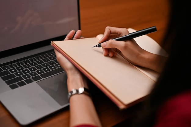 A businesswoman writing or taking notes something on her blank notebook at her office desk