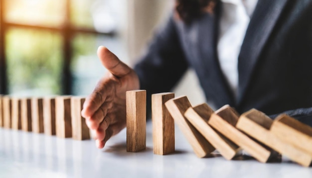 businesswomans hand halts a cascade of falling wooden dominoes symbolizing risk management and fin