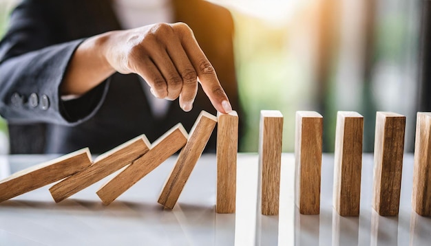 businesswomans hand halts a cascade of falling wooden dominoes symbolizing risk management and fin