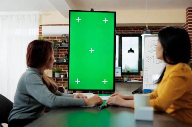 Businesswomen looking at green screen chroma key mock up vertical monitor with isolated display working at management strategy. Entrepreneurs working in startup business company office