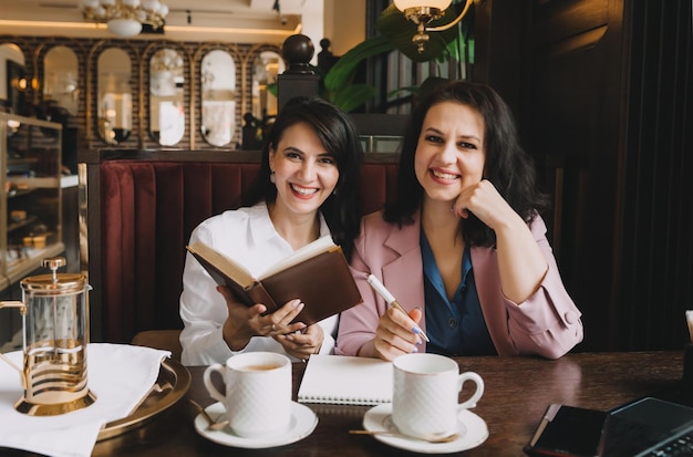 Businesswomen sit in a cafe drink coffee and have a business conversation discuss business and have fun