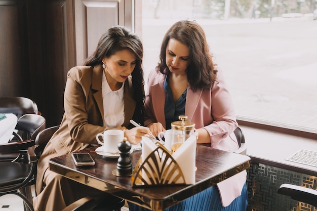 Businesswomen sit in a cafe drink coffee and have a business conversation discuss business and have fun