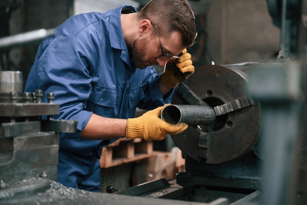 Photo busy by working with automatic machine man at factory and in blue uniform is indoors