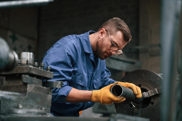 Photo busy by working with automatic machine man at factory and in blue uniform is indoors