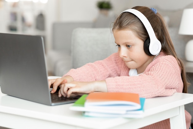 Busy concentrated caucasian small girl in headphone types do homework watches video lesson