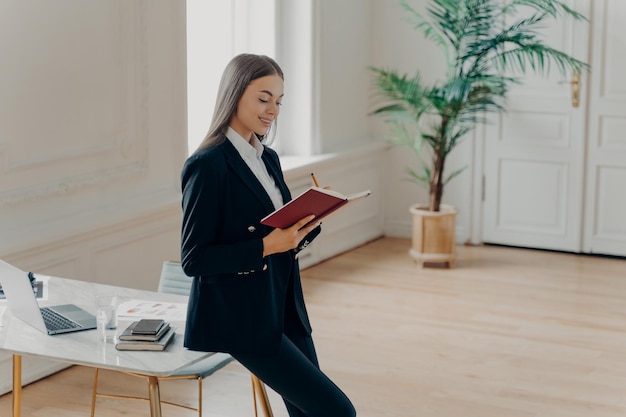 Busy female director planning working day while leaning on desk in her cabinet