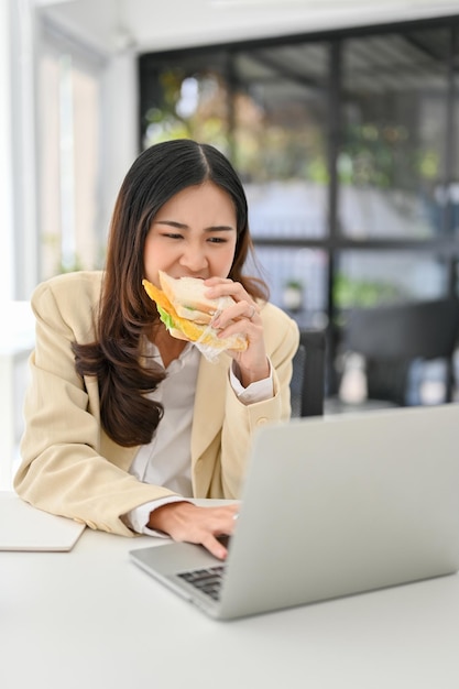 Busy and hardworking Asian businesswoman eating a sandwich while working on her project