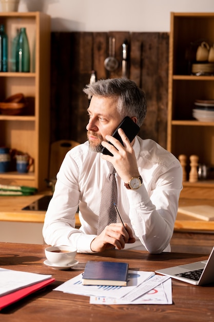 Busy man talking by phone in kitchen