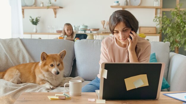 Busy mom trying to work remotely from home in the background her daughter is seated at a desk while ...