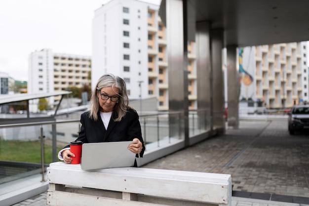 Busy successful mature adult female boss standing with laptop in the street