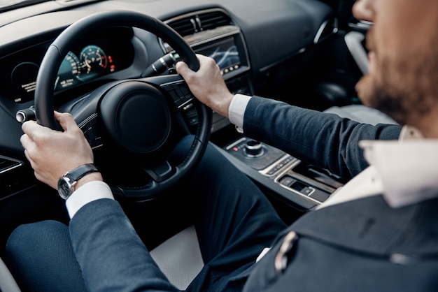 Busy working day. Close up top view of young man in formalwear keeping hands on the steering wheel while driving a luxury car