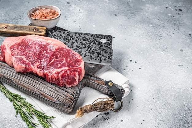 Butcher board with Raw striploin beef meat steak on wooden cutting board Gray background Top view Copy space