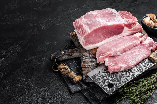 Butcher board with sliced raw pork loin fillet ready for cooking chop steaks Black background Top view Copy space