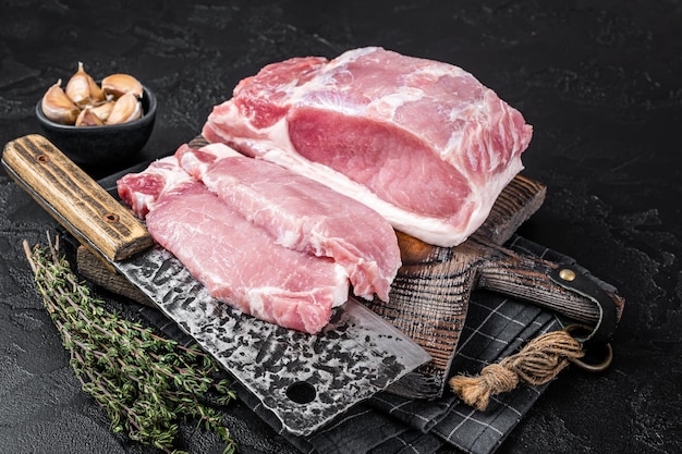 Butcher board with sliced raw pork loin fillet ready for cooking chop steaks Black background Top view