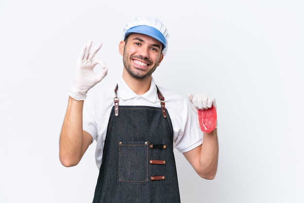 Butcher caucasian man wearing an apron and serving fresh cut meat over isolated white background showing ok sign with fingers