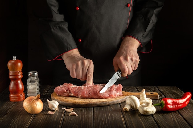 Butcher or chef cuts raw veal meat on a cutting board before barbecue