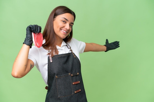 Butcher woman wearing an apron and serving fresh cut meat isolated on green chroma background extending hands to the side for inviting to come