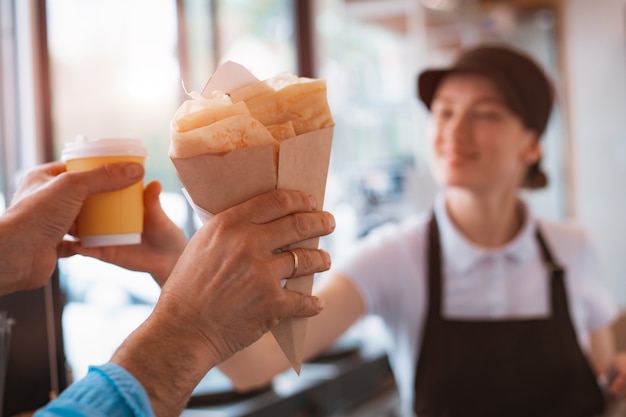 Buying fast food. A pancake with filling and a paper cup with coffee in the hands of a woman seller and a customer in the cafeteria. Takeaway food.