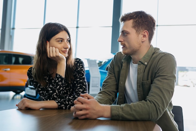 Buying a new family car A young couple is sitting at a table in a dealership