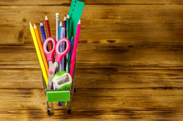 Buying school supplies Shopping cart with school supplies on a wooden background Back to school concept