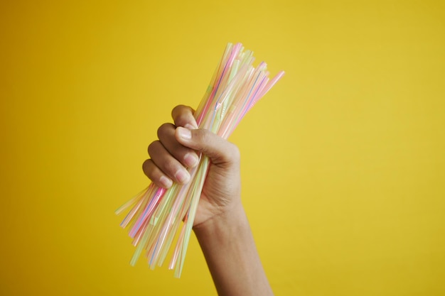 C holding many plastic straws against yellow