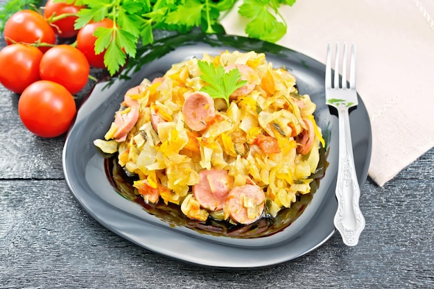 Cabbage stew with sausages in plate on dark board