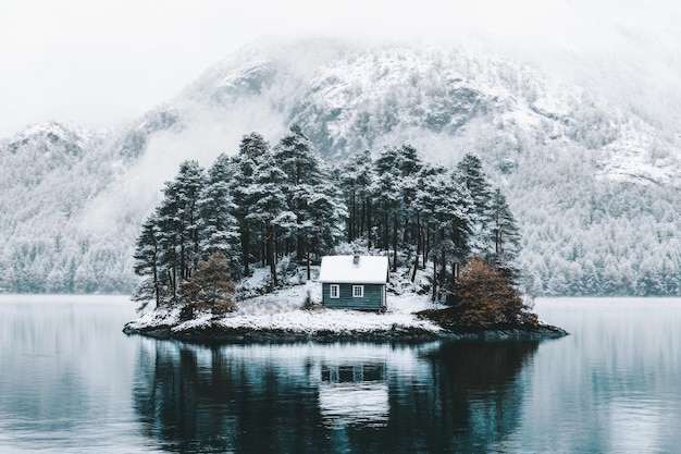 The cabin is on an island on a frozen lake with trees and a snowy pine forest in the background on a cloudy day at lake Eibsee Germany