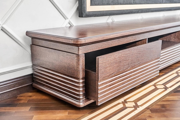 Cabinet for TV set made of veneer and solid oak lumber toned in dark brown color near molded wall