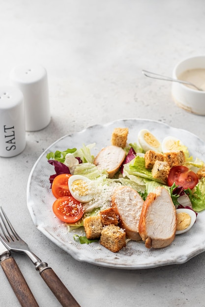 Caesar salad Healthy salad made with chicken fillet cherry tomatoes iceberg lettuce parmesan cheese and croutons on light grey background with cutlery Light diet dinner text space