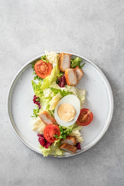 Caesar salad in modern linear feed with chicken egg tomatoes lettuce and parmesan chips isolated on gray table top view flat lay text space menu