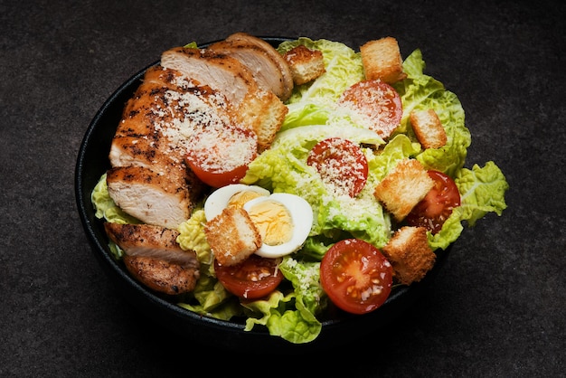 Caesar salad with chicken breast, cherry tomatoes and parmesan on a dark background, close up